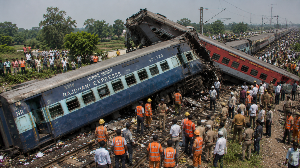 2002 की रफीगंज राजधानी एक्सप्रेस रेल दुर्घटना (बिहार) का यथार्थवादी चित्र, जिसमें पटरी से उतरी राजधानी एक्सप्रेस के क्षतिग्रस्त डिब्बे, बचाव अभियान और राहतकर्मी दिखाई दे रहे हैं।